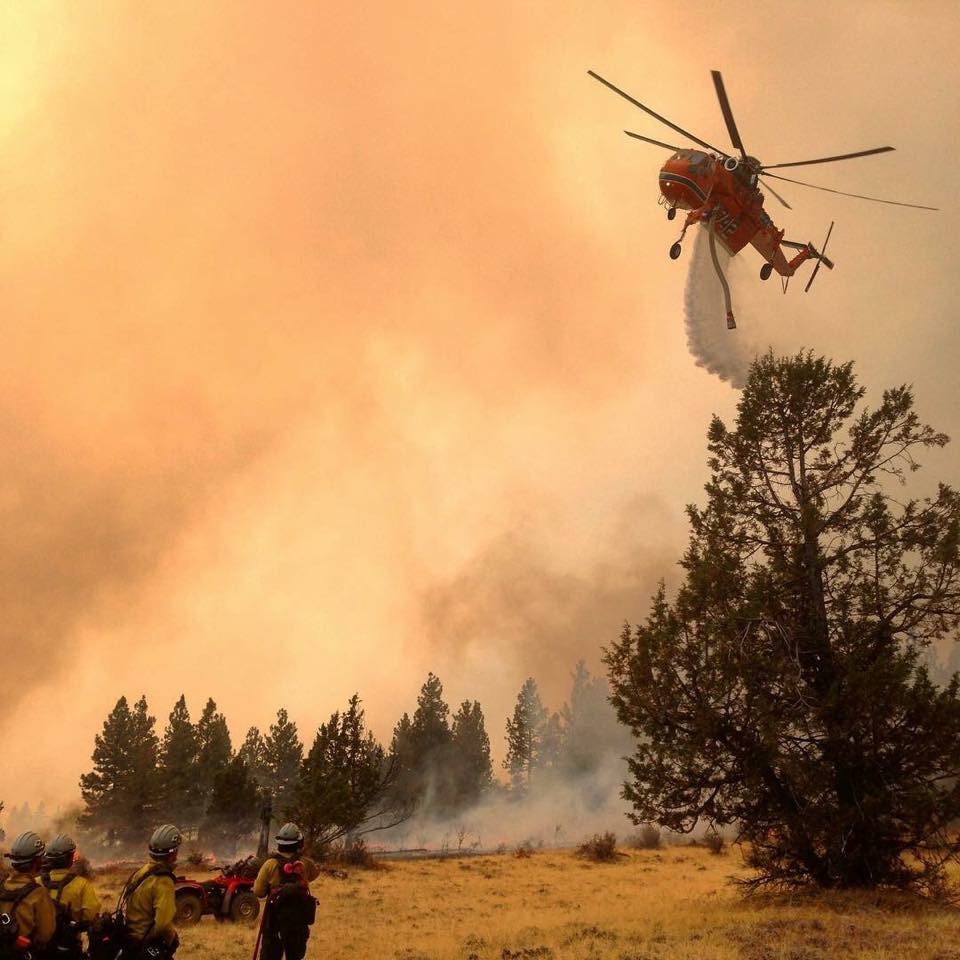 Image of a helicopter tanker dropping water on a spot fire.