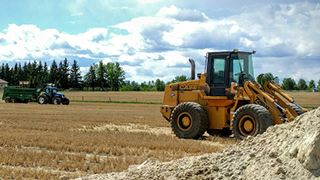 Image of tractors moving across a field under a cloudy blue sky.