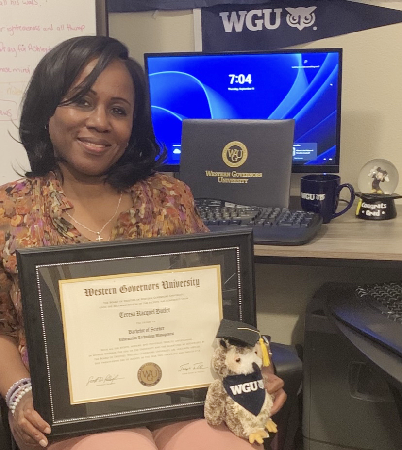 Image of Teresa holding her college degree while sitting in front of a computer.