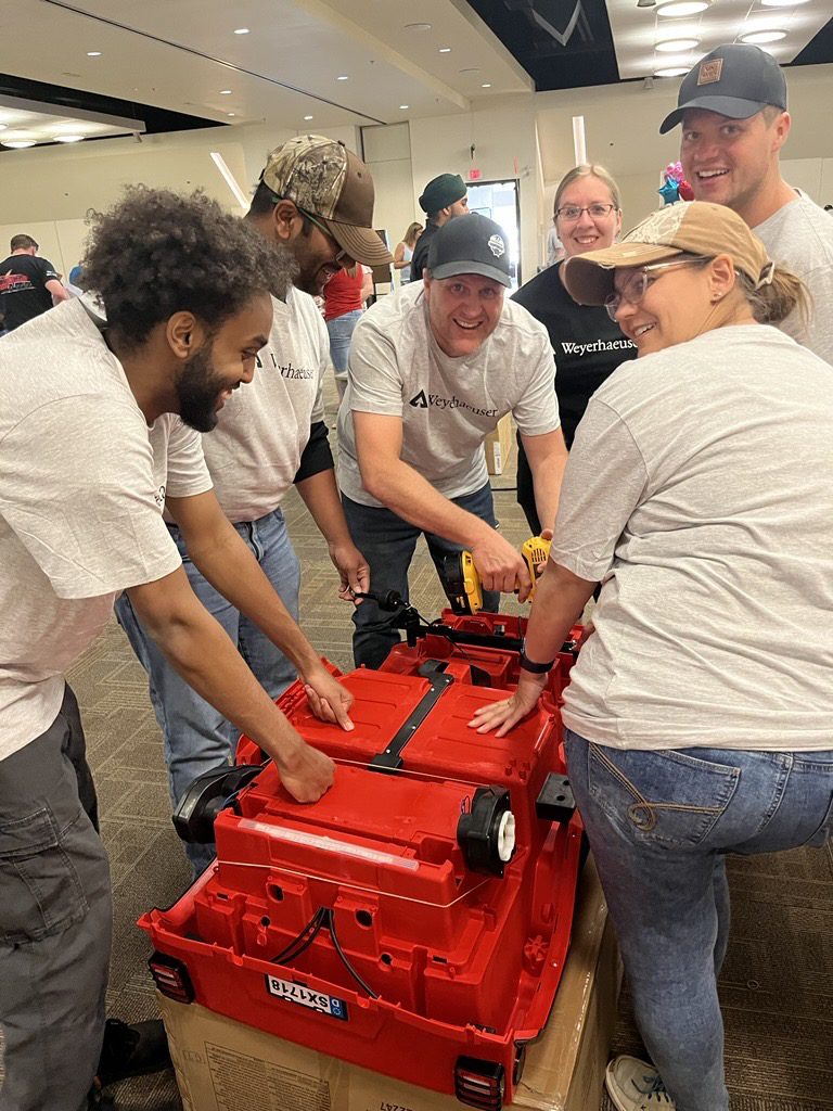 Image showing Matt with a number of colleagues after assembling a rideable car for a local child. The car is red and all of the team members are surrounding the vehicle..
