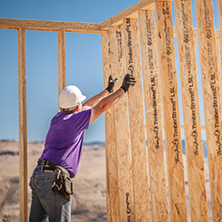 Image of a man in a purple shirt with a hardhat and other PPE gear holding up a frame that was constructed with TimberStrand LSL framing.