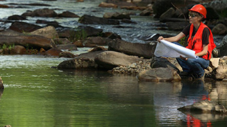 Link to Water Use section of Data and GRI Index page, with image of person in hardhat and orange vest looking at waterway and examining data