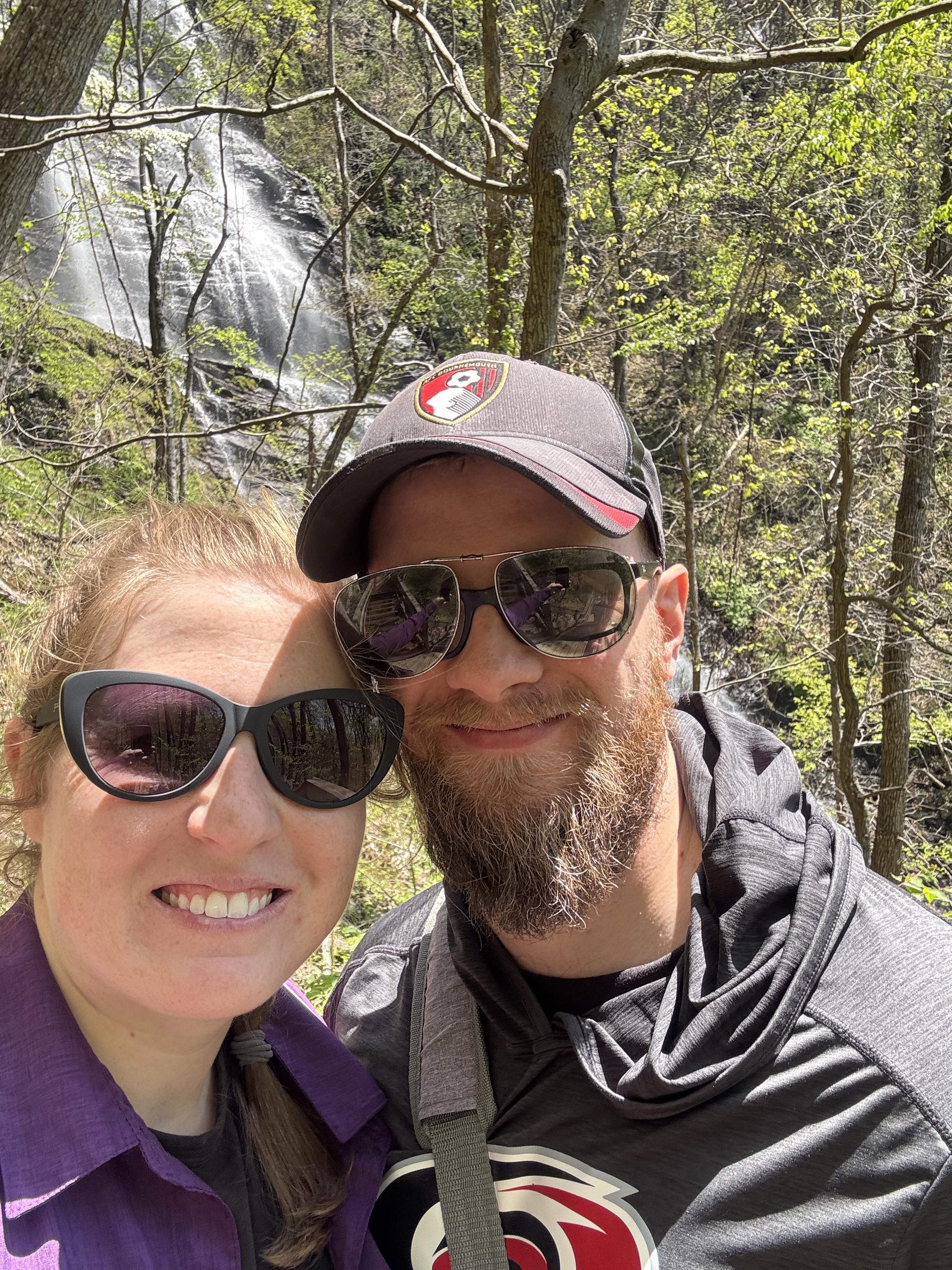 Image of Jaine with her boyfriend, Jonathan. They are standing in among a group of trees and a stream and small waterfall are seen in the background.