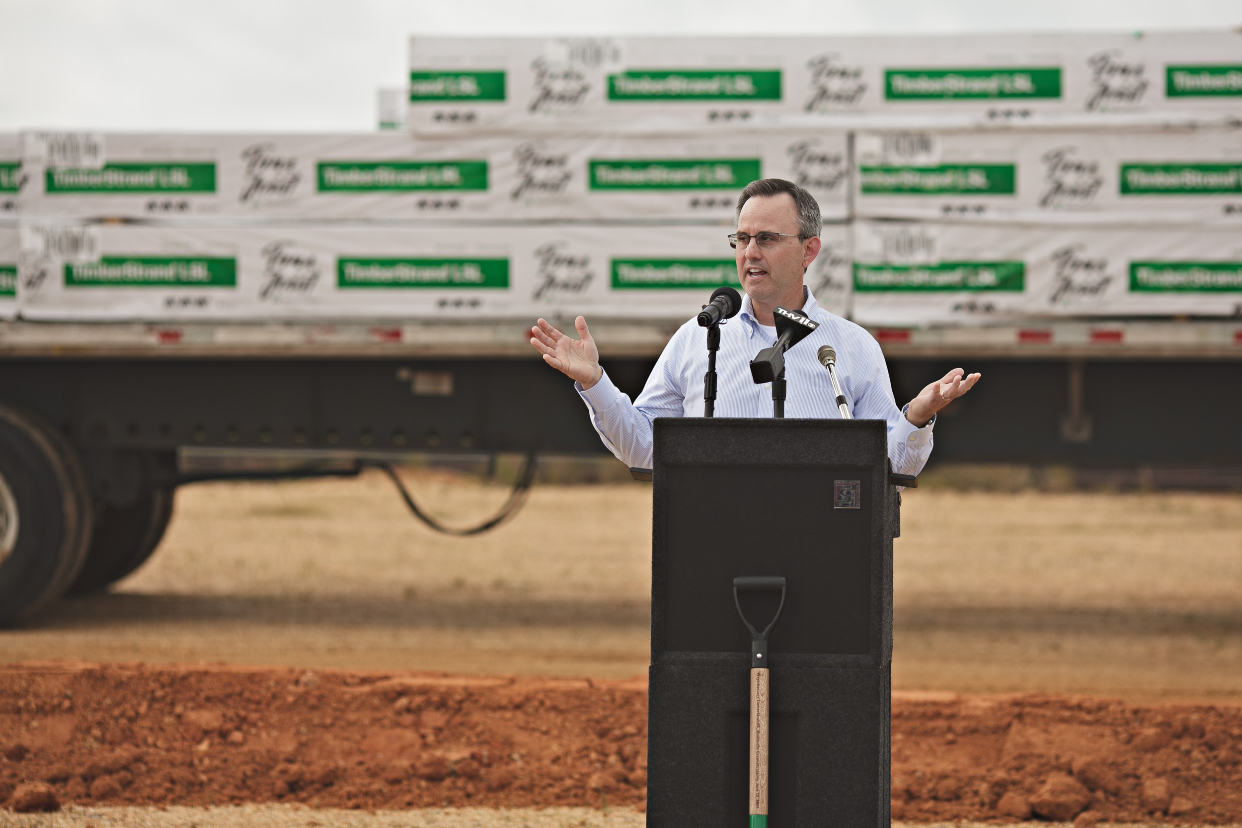 Imge of Devin Stockfish speaking during the ceremony. He is at a podium with microphones, and in the background are stacks of TimberStrand.