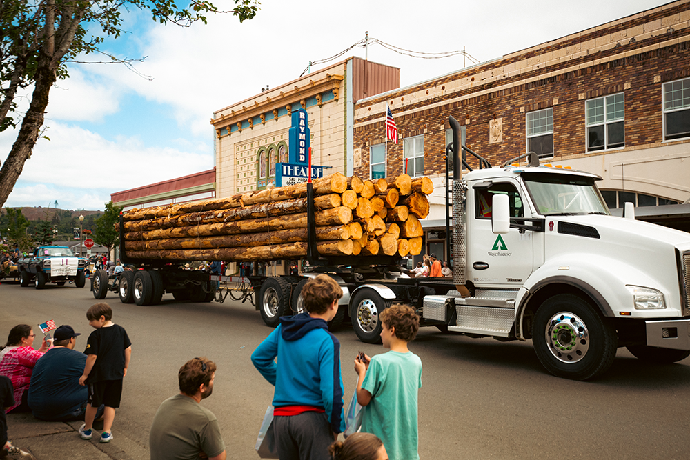 A large truck carrying logs goes down the street during the Willapa Harbor Festival.