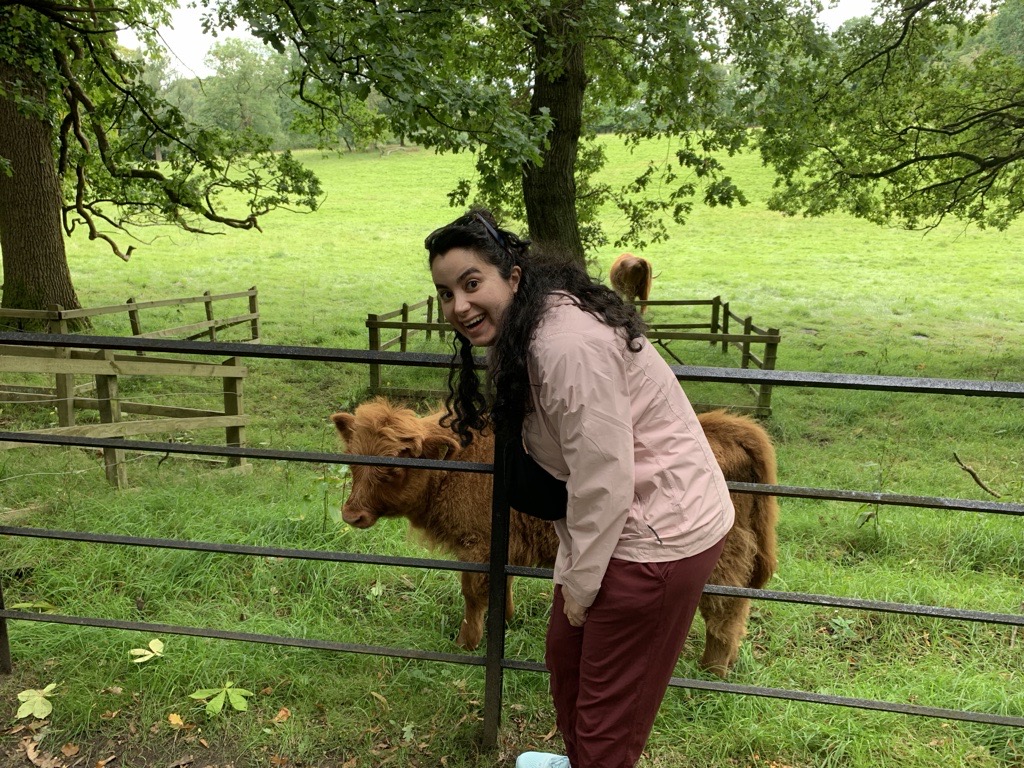 Image of Neda standing at a gate with a highland cow on the other side.