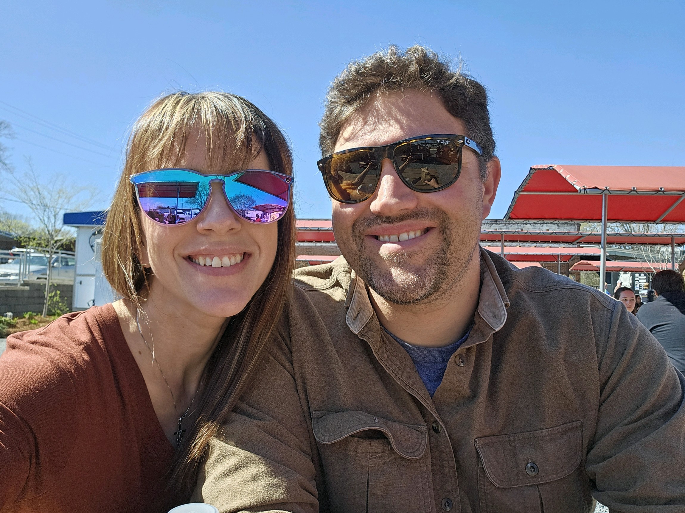 Image of Seth and Heather enjoying a kid-free lunch in Ruston, Louisiana. Both are wearing sunglasses and smiling broadly. The sky in the background is blue and cloudless. 