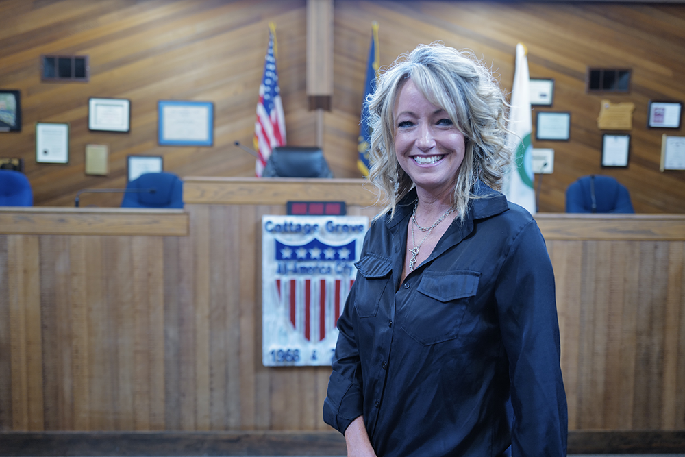 A spectator smiles as her picture is taken. She has long blonde hair and a black shirt.