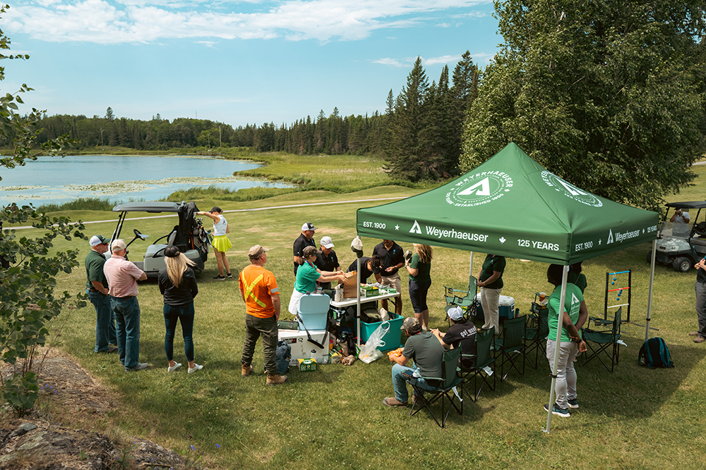 Image of a group of people standing under and near a Weyerhaeuesr tent.
