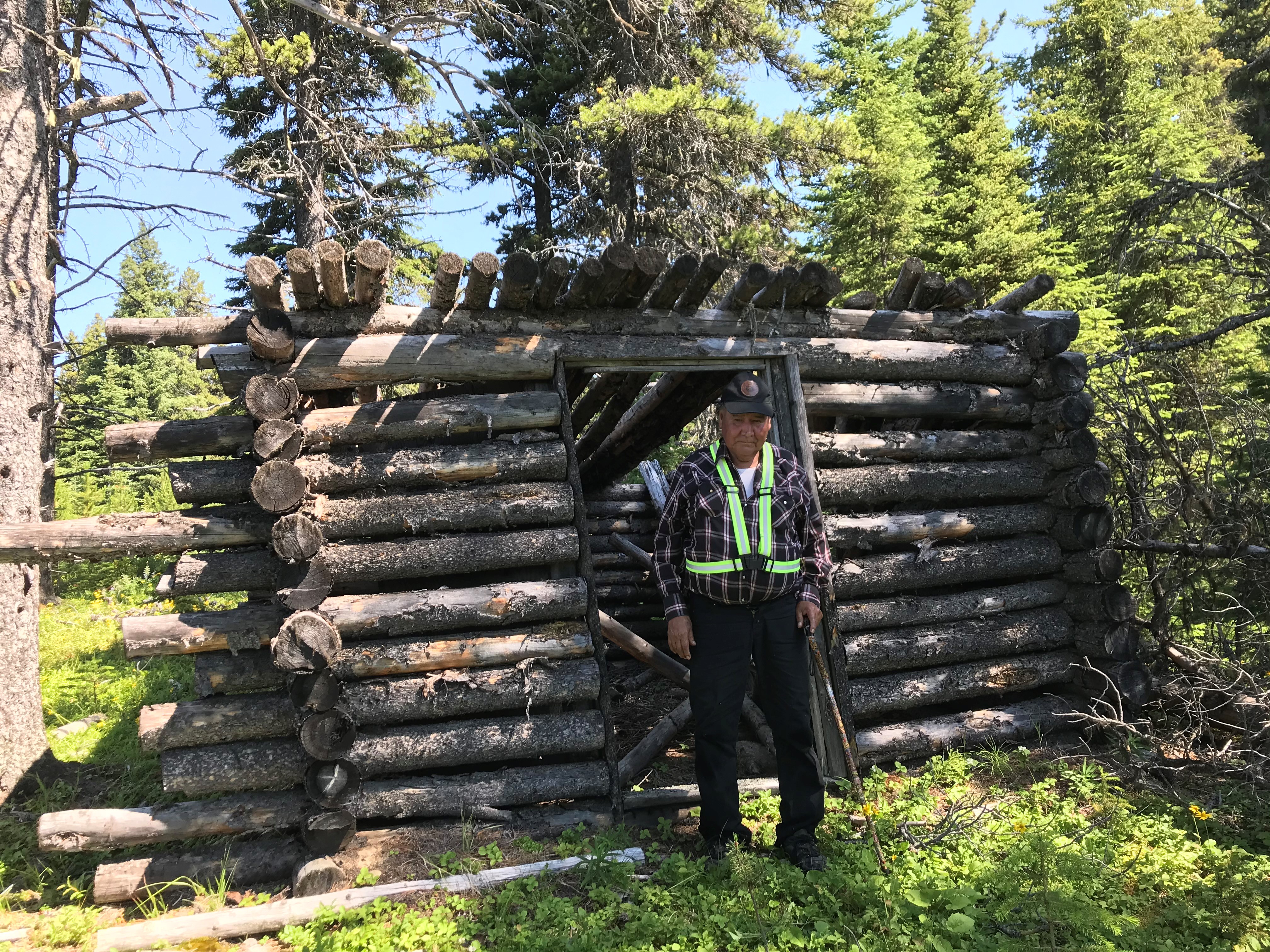Image of AWN Elder Roland Karakuntie standing in front of a cabin he built many decades ago for hunting and trapping.