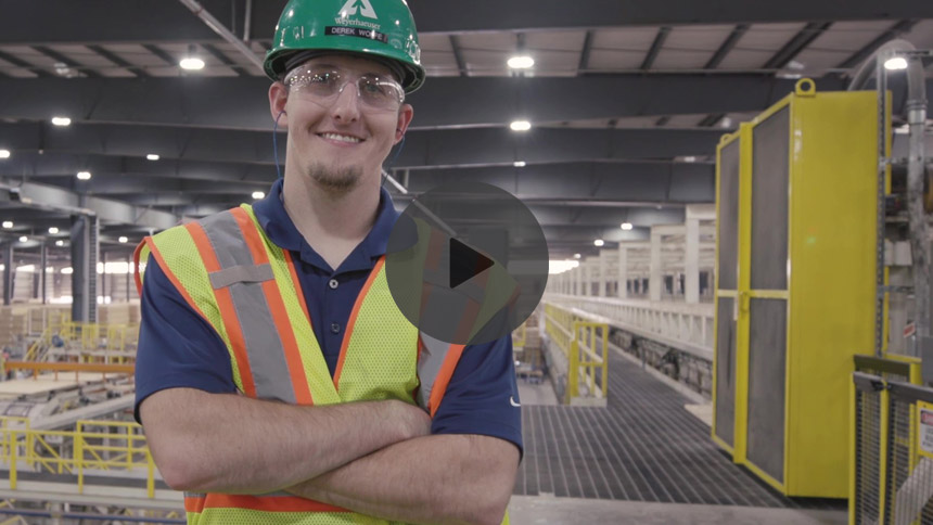 Image of a smiling employee in a green hardhat in a factory.