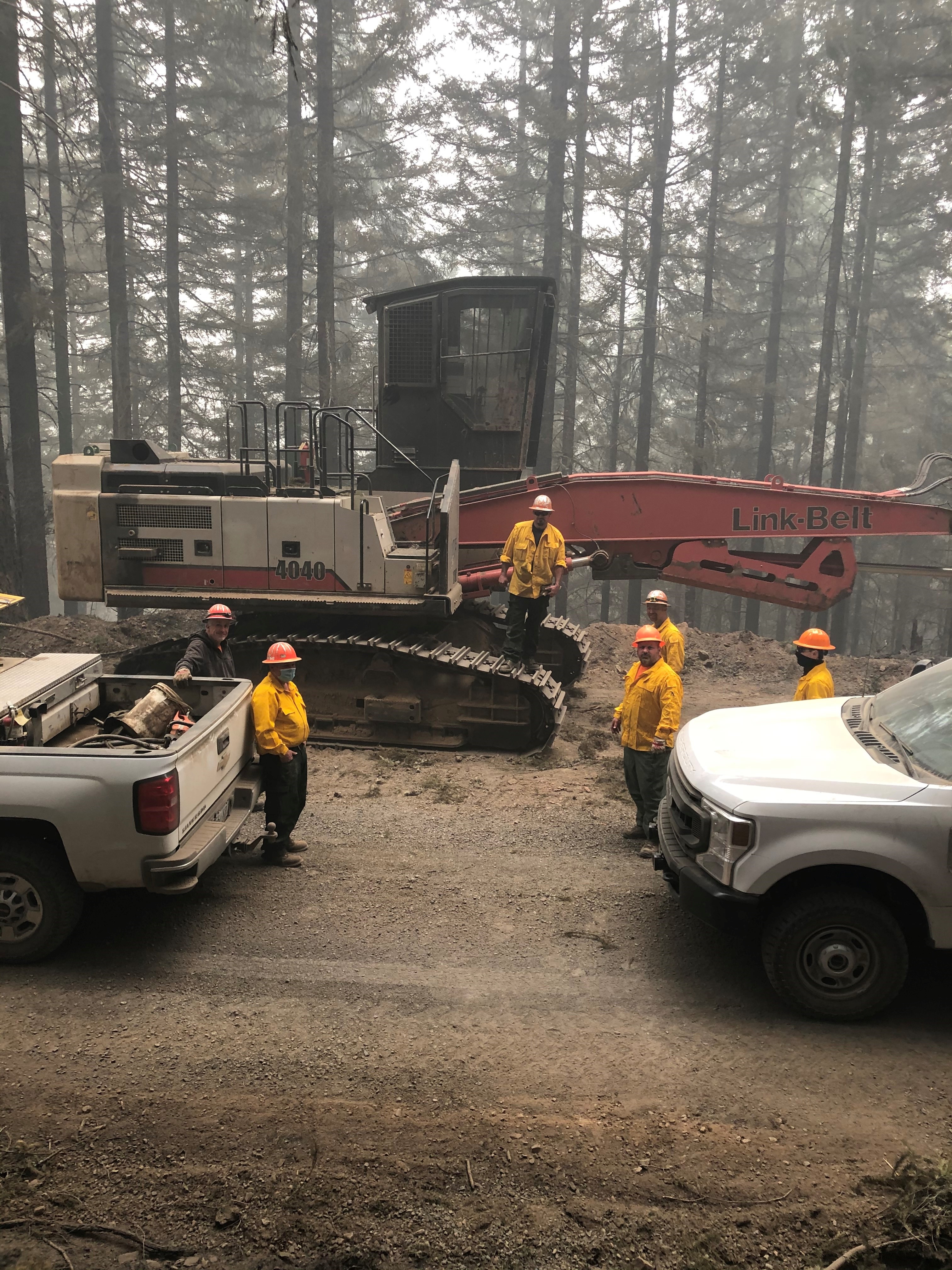 Image of vehicles and large equipment gathered at the swide of a road with firefighters preparing to fight a fire.