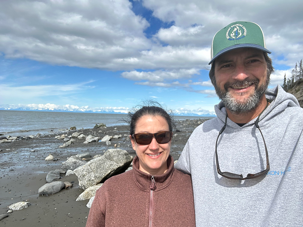 Kelly and her husband stand along the coastline in Alaska.