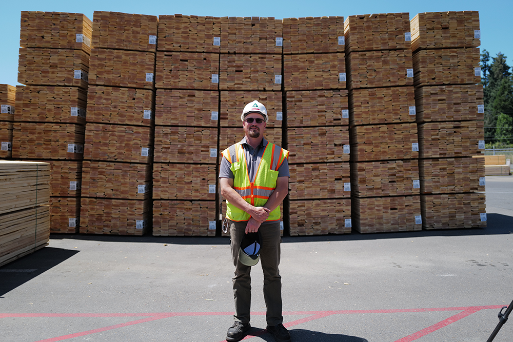 image of a Weyerhaeuser employee standing in a lumber yard in front of stacks of wood that are ready to be shipped.