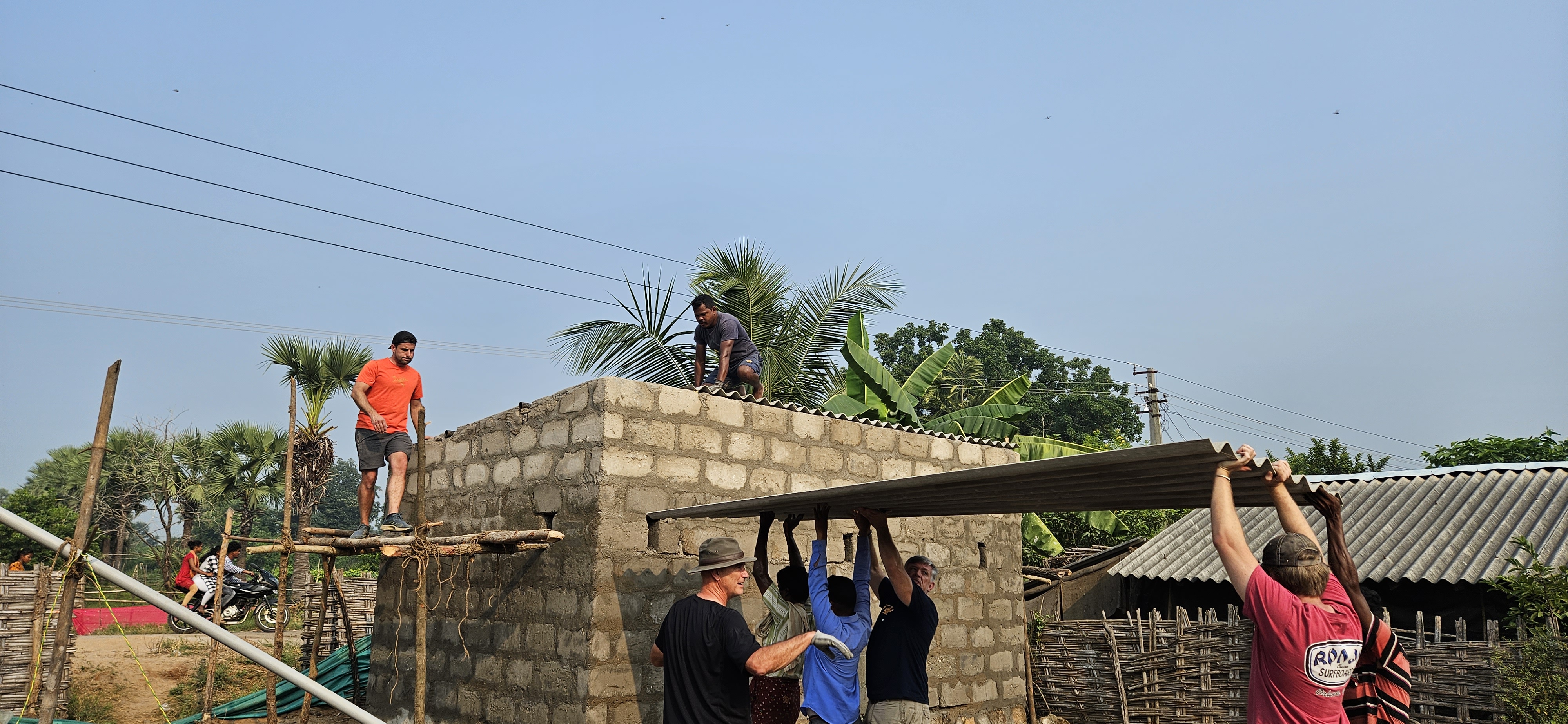Image of Aasha volunteers lifting the last piece of roofing material to the top of the building that houses the water filtration system they installed.