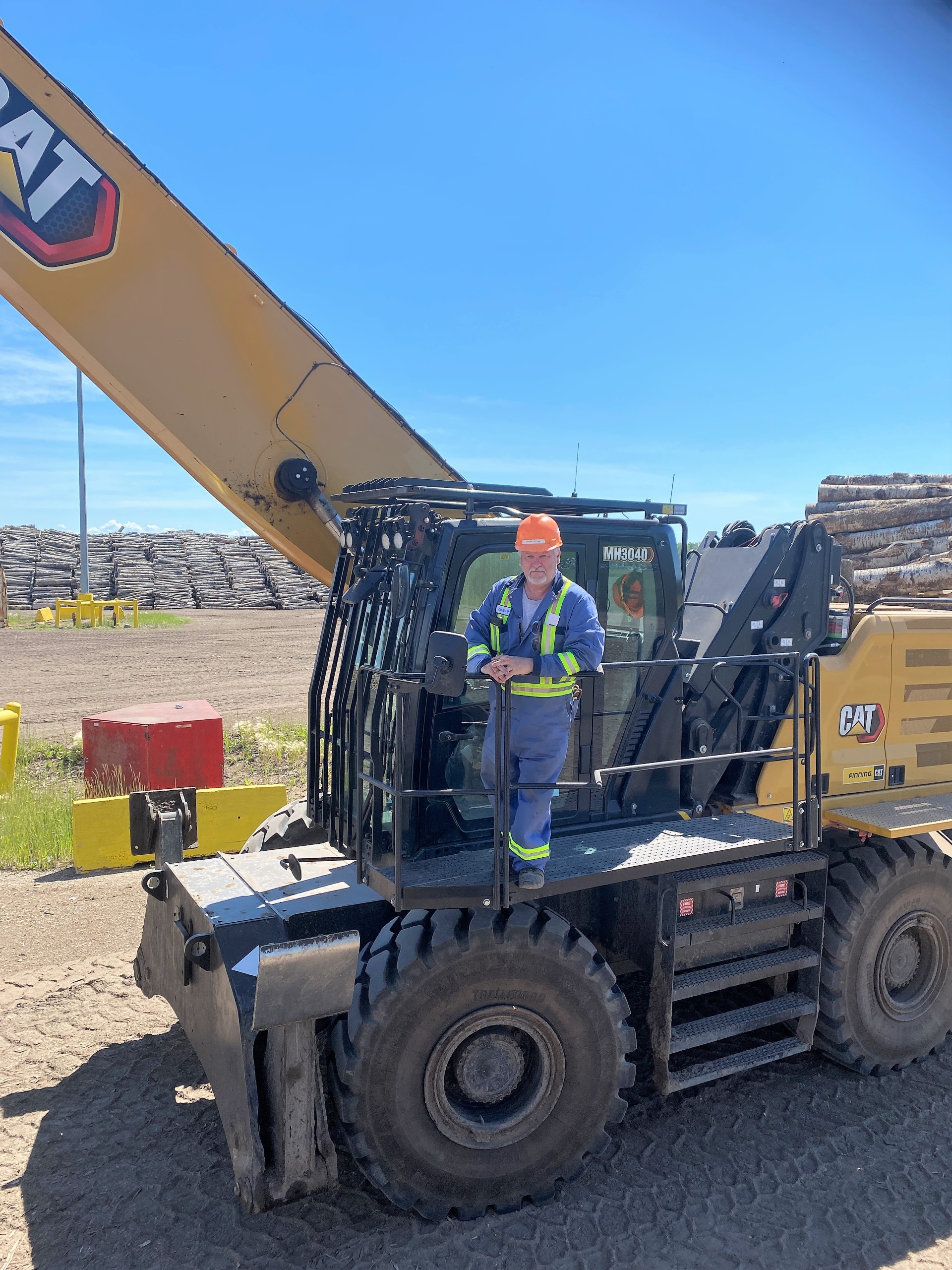 Darwin stands outside the cab of his CAT 3040 in Hudson Bay's log yard.