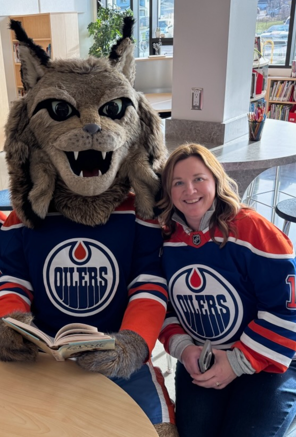 Image of Kerri wearing an Edmonton Oilers jersey while posing with the Oilers mascot, Hunter the Lynx.
