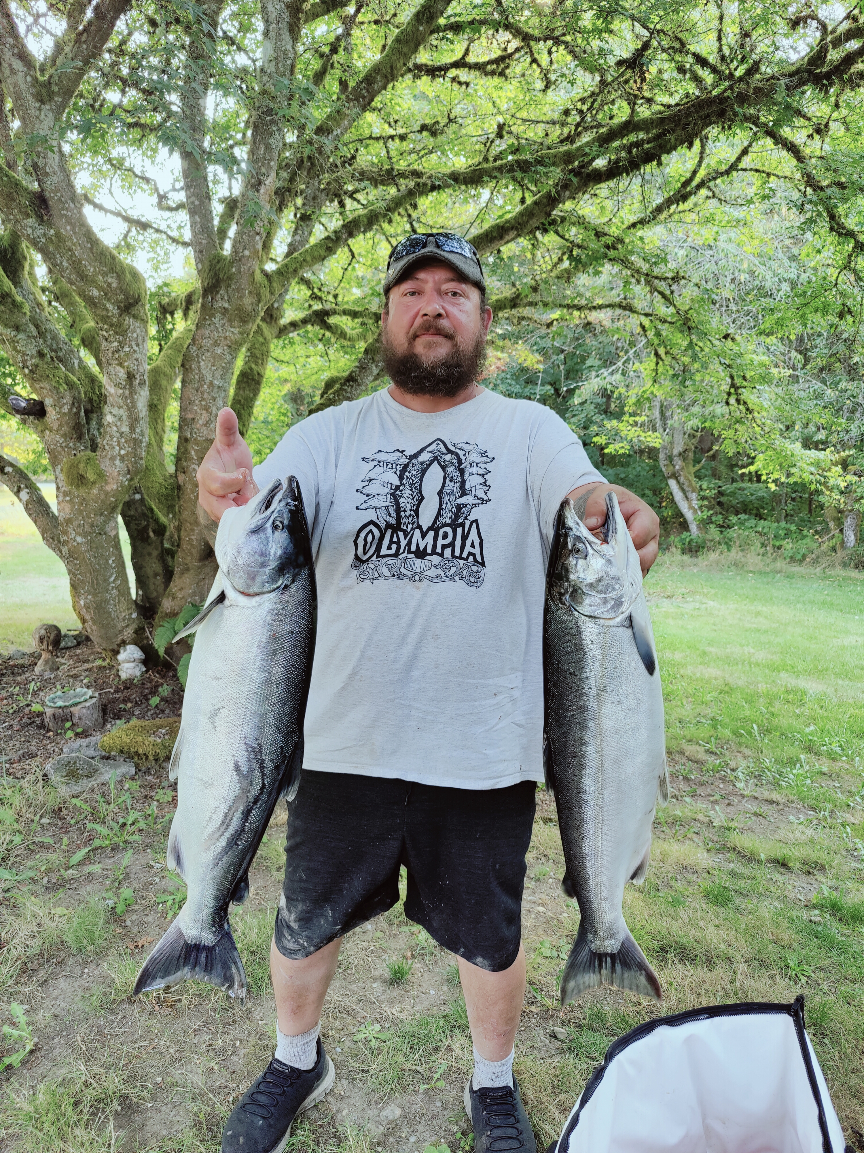 Bob is pictured holding two massive fish. Bob is wearing a gray shirt that says "Olympia," and black shorts. 