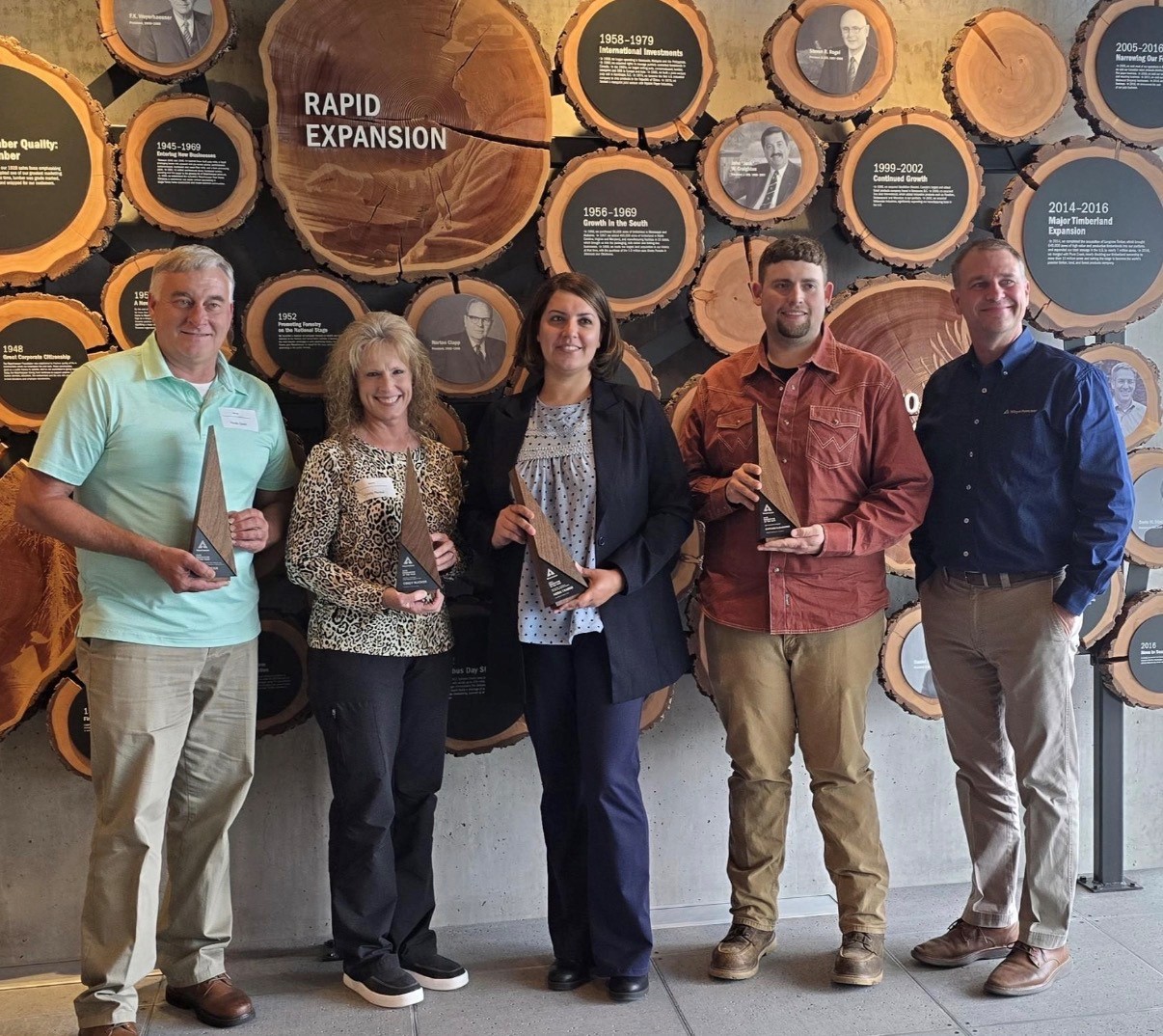 Image of Cindy and other innovator of the year winners standing in front of a wall showing the history of the company at the headquarters in Seattle.