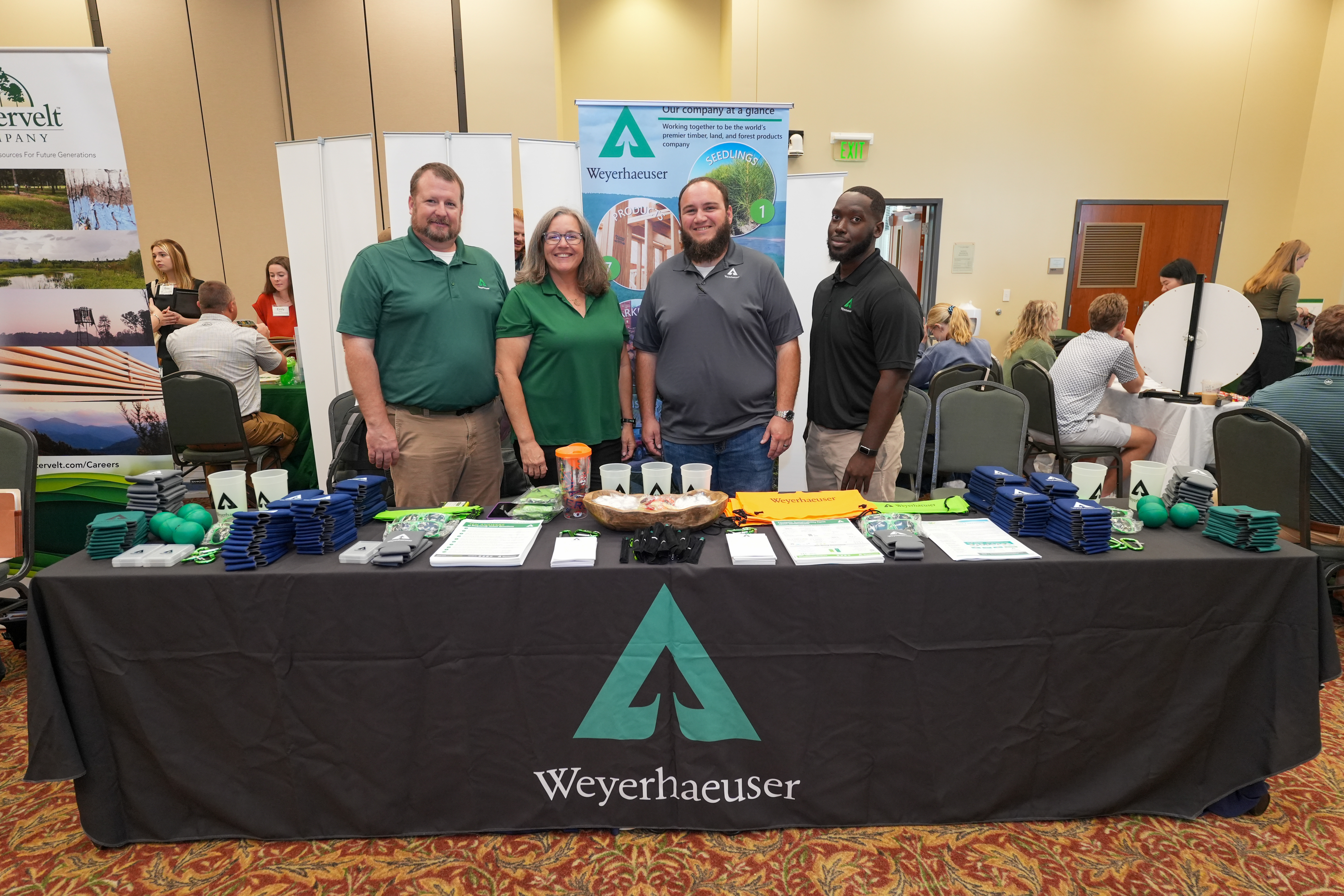 Image showing a Weyerhaeuser-themed booth with several employees wearing Weyerhaeuser shirts. Marquess is on the left side of the picture.