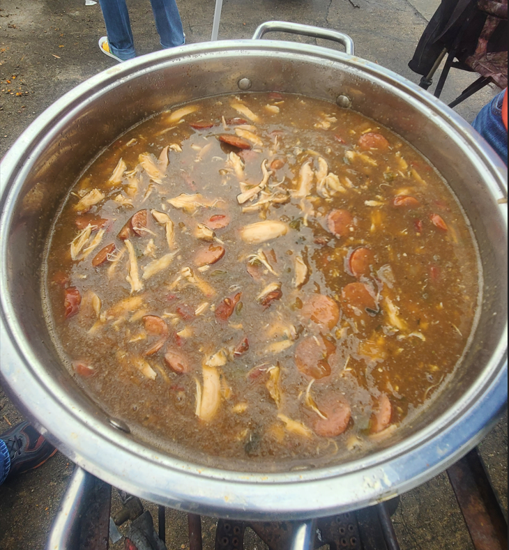 Imag eof a finished pot of gumbo, ready to be tasted. Visible are andouille sausate and shredded chicken in a red sauce.