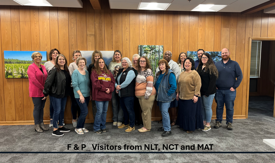Image of Cindy and other finance and planning managers in the company's Hot Springs, Ark., office. The office is wood-panelled and the group is all posing together.