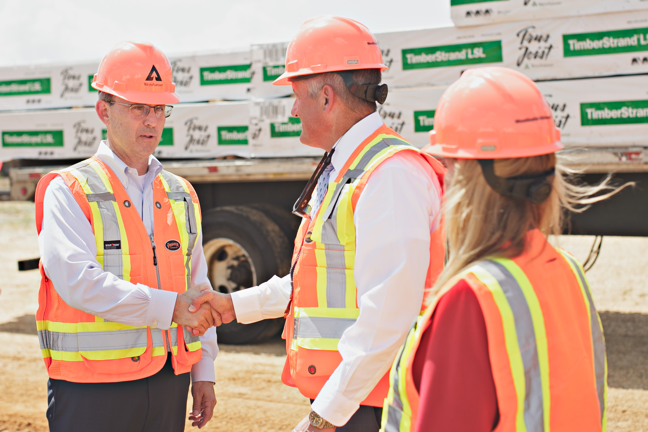 Image showing Devin Stockfish and several others in personal protective gear shaking hands after the ceremonial groundbreaking. They are each wearing orange hardhats and safety vests.