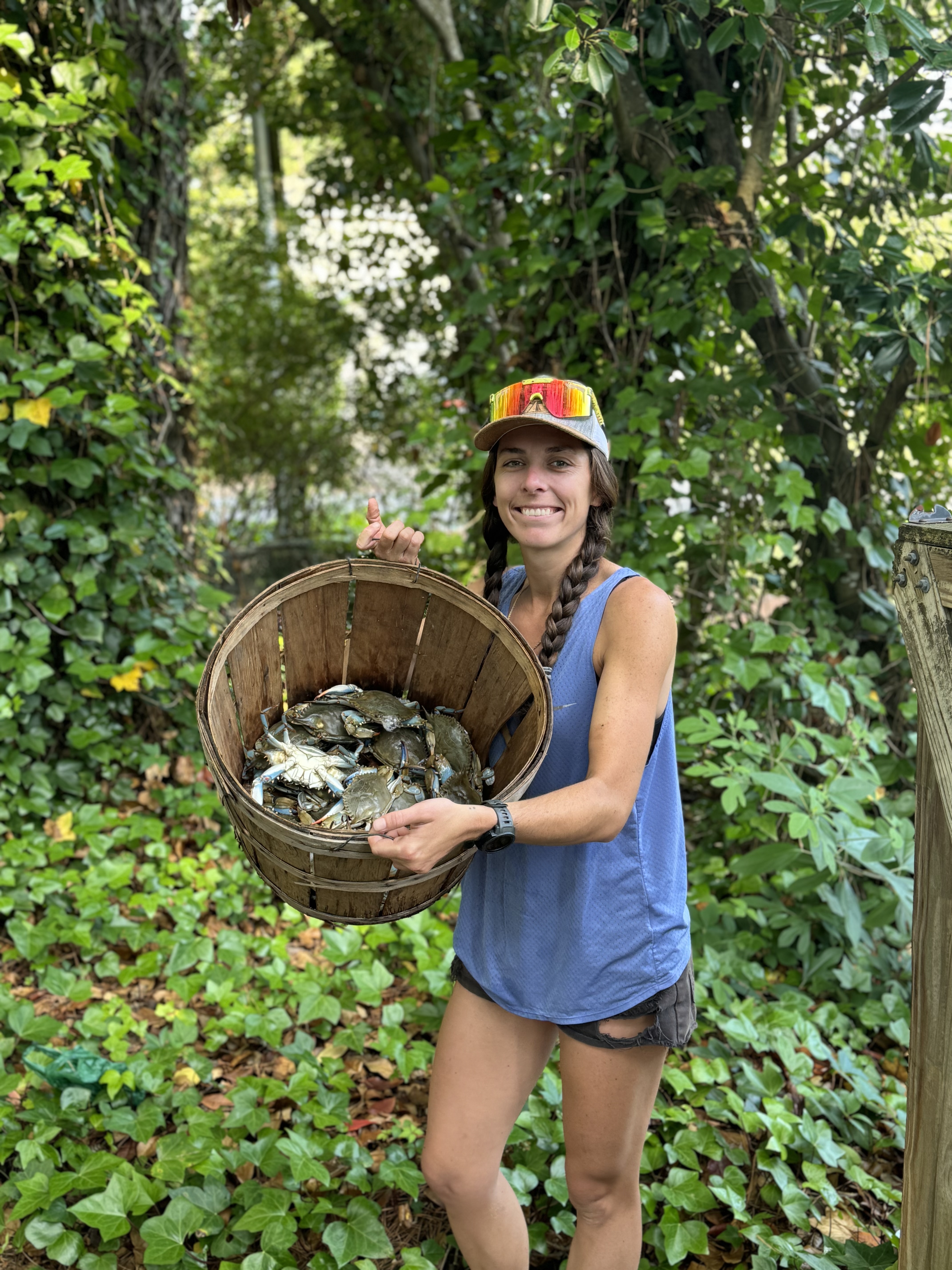 Image of Catherine holding a basket with crabs in it. Catherine is wearing shorts and a tank top, as well as a baseball cap.
