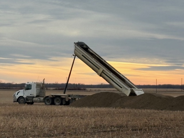 Image showing a dumptruck with its bed tilted to allow the ash to fall onto the ground. The ash is then spread to allow it to neutralize acidic sils as a liming agent.