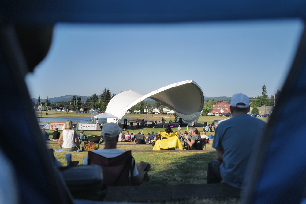 Image of the concert venue seen from the distance, as people sit on the lawn in front of it to watch the show.