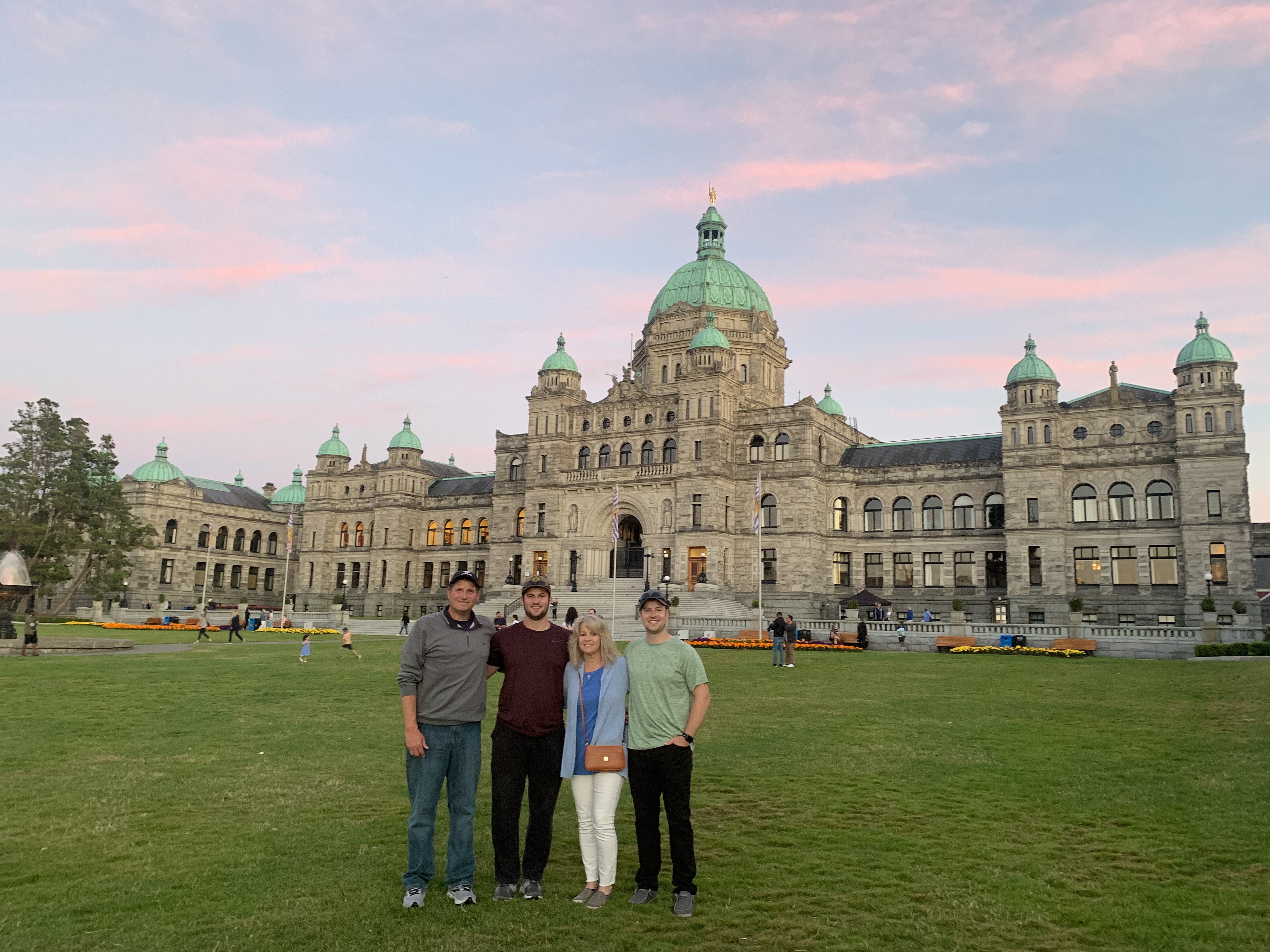 Tim stands with his family stand in front of the British Columbia Parliament Buildings in Victoria, BC.