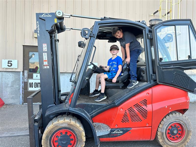 Image of Reid Peace and Braxton Harder playing in the Linde foreklift that Dave Byzuk safety set up to showcase in the kids zone.