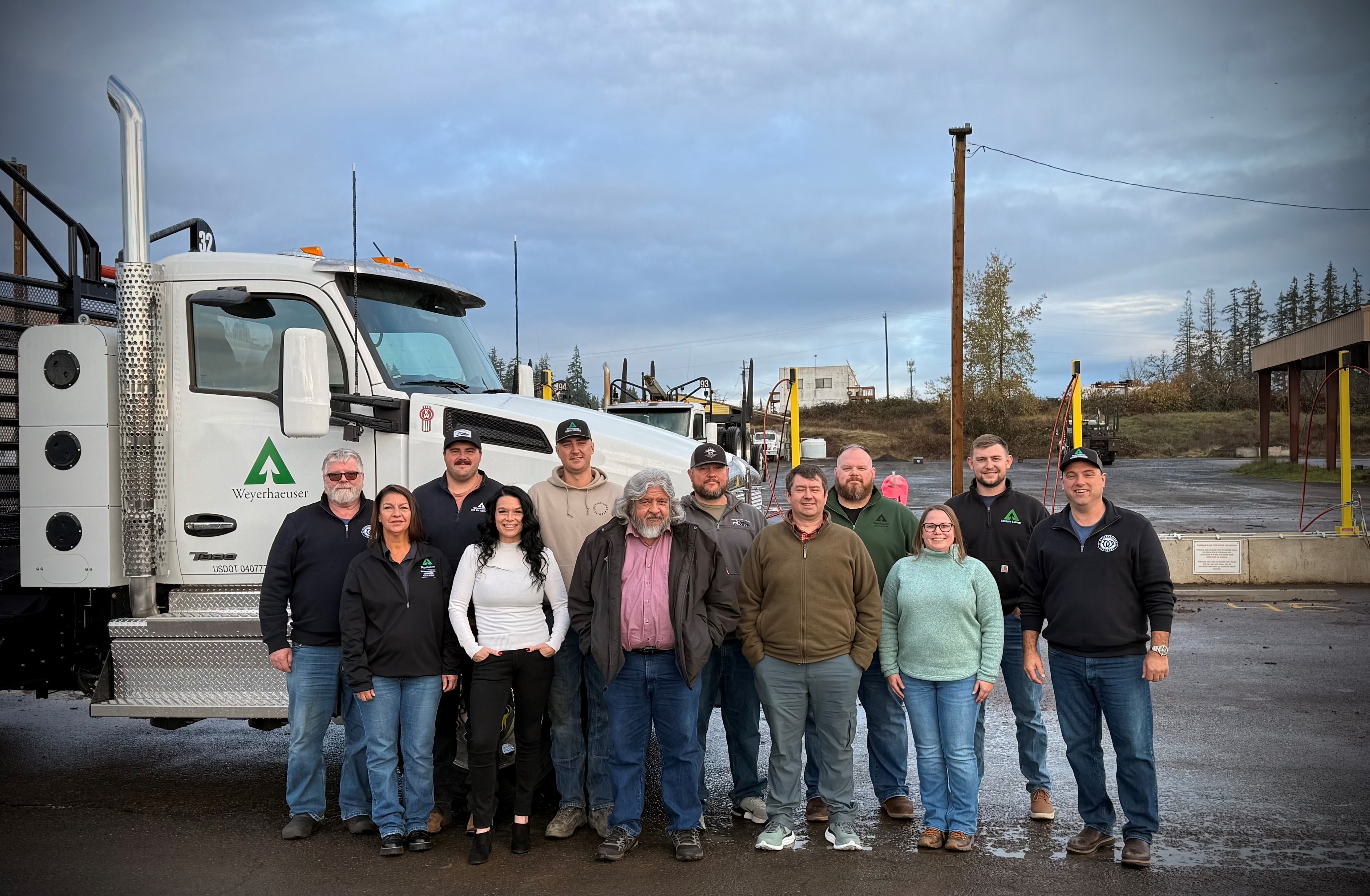 A large group of Weyerhaeuser employees stand in front of the natural gas-powered log truck.