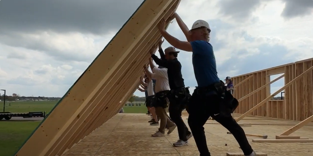 Image of student volunteers working together to raise a wall.