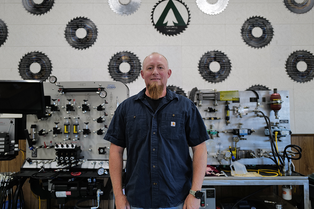 Image of a Weyerhaeuser employee standing in a workshop in front of a wall with numerous saw blats on it.