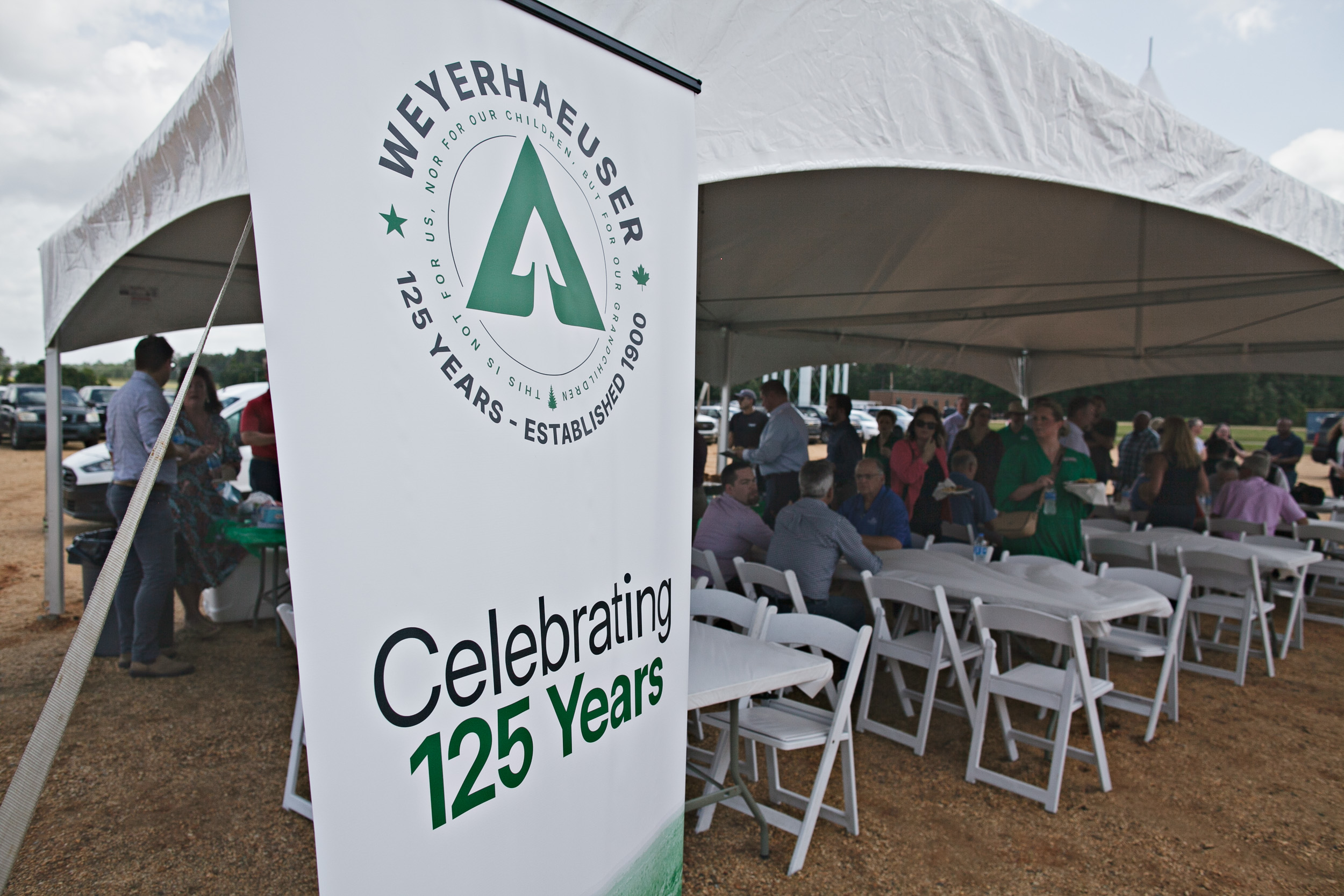 Image of a sign in front of a tented area that says "Weyerhaeuser Cebrating 125 Years."