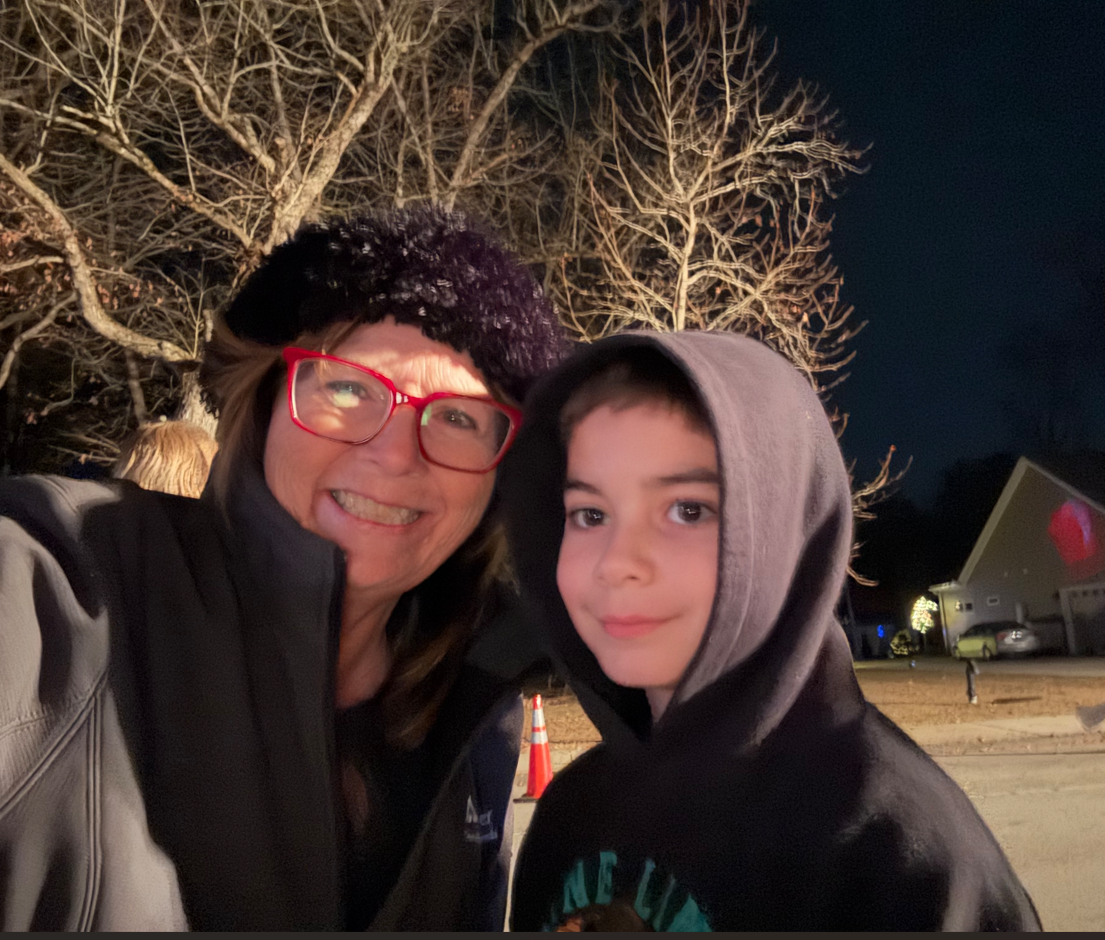 Image of Lori and her grandson Gavi. This selfi shows Lori on the left wearing a jacket and black hat with glasses with red frames. Her grandson is to the right wearing a black hoodie with the hood over his head.