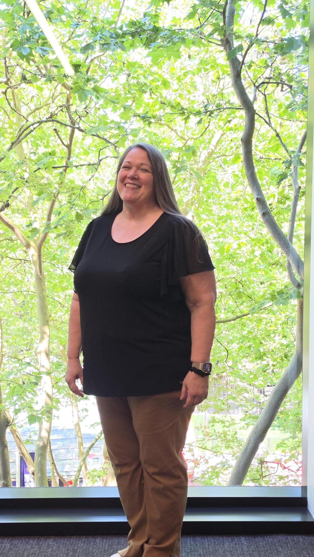 Image of Torri at Seattle headquarters. She is standing in front of a large window and is wearing a black blouse.