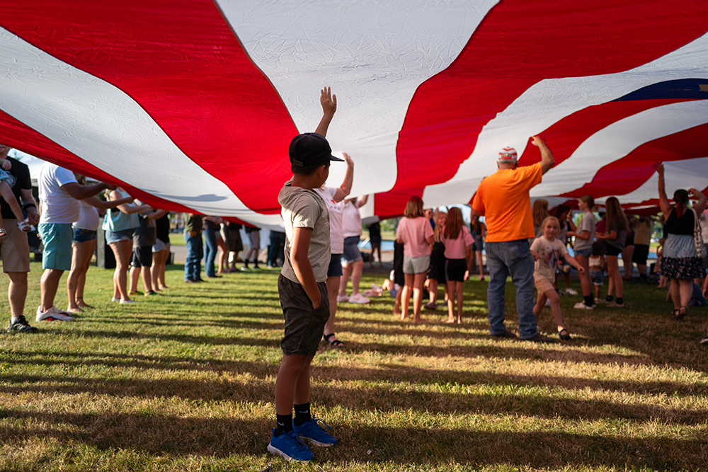 Image of a child standing under a massive flag of the United States of America.