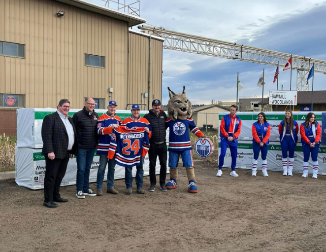 Image of Edmonton Oilers Kevin Lowe and Ben Scrivens, wearing their Oilers jerseys, along with Weyerhaeuse3r representatives and the Oilers mascot standing outside the Drayton Valley mill.
