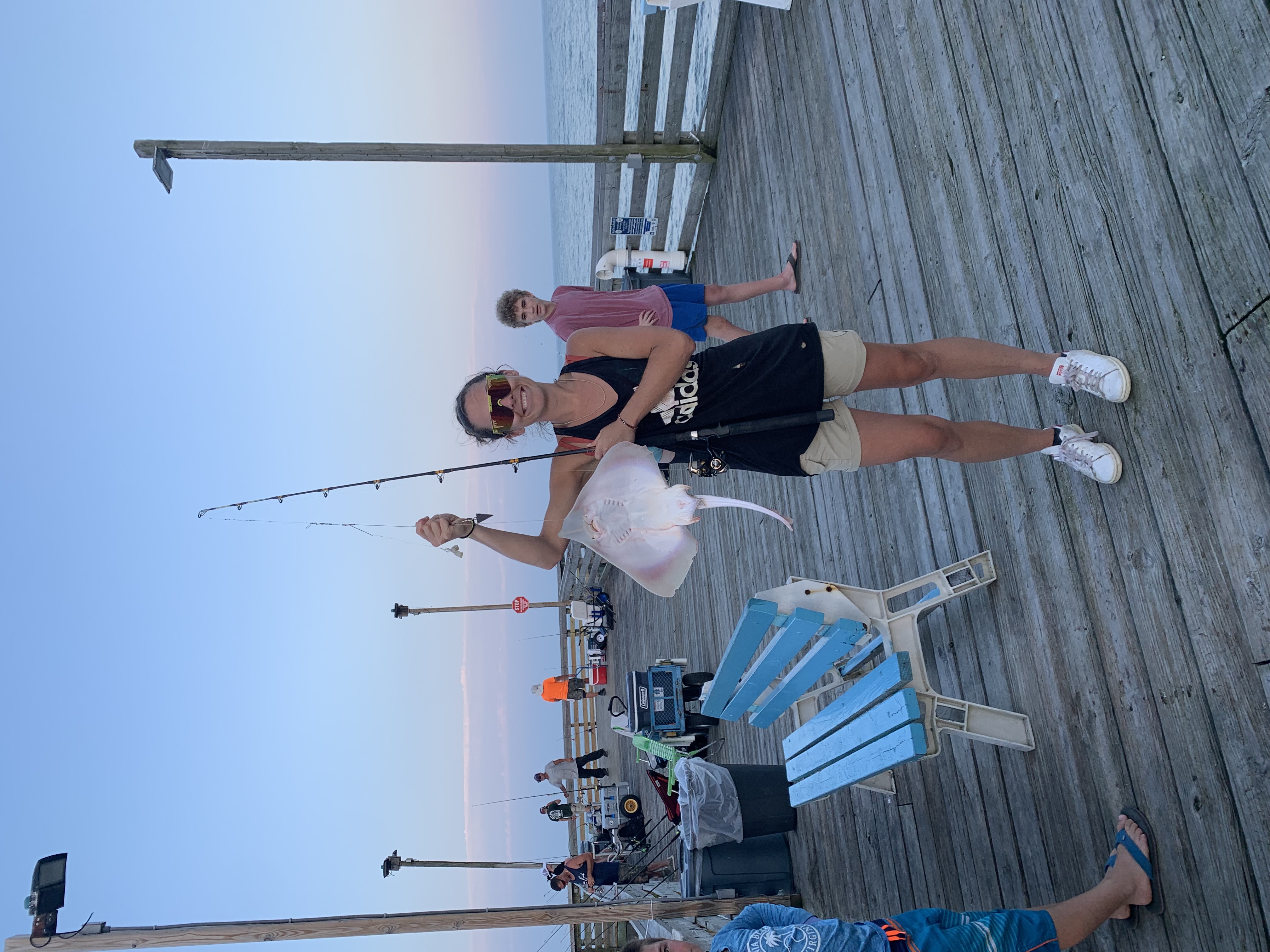 Image of Catherine standing on a pier holding a fishing rod and showing off a fish she caught.