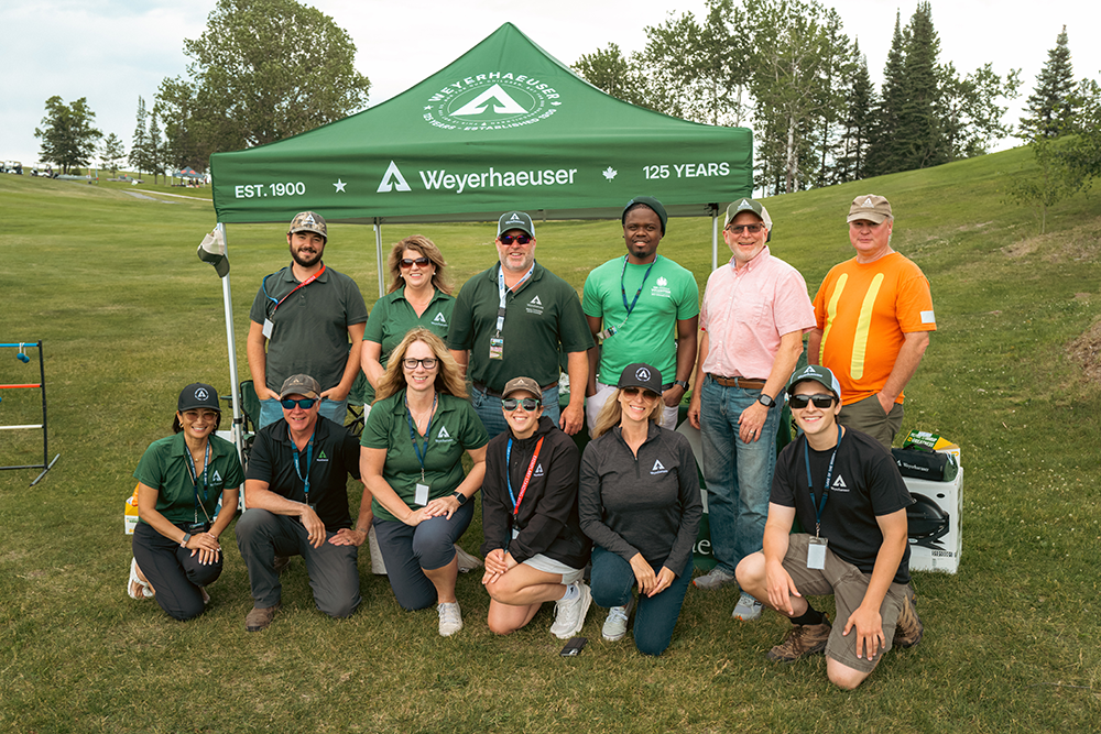 Image of about a dozen people posing in front of a Weyerhaeuser tent on a golf course.