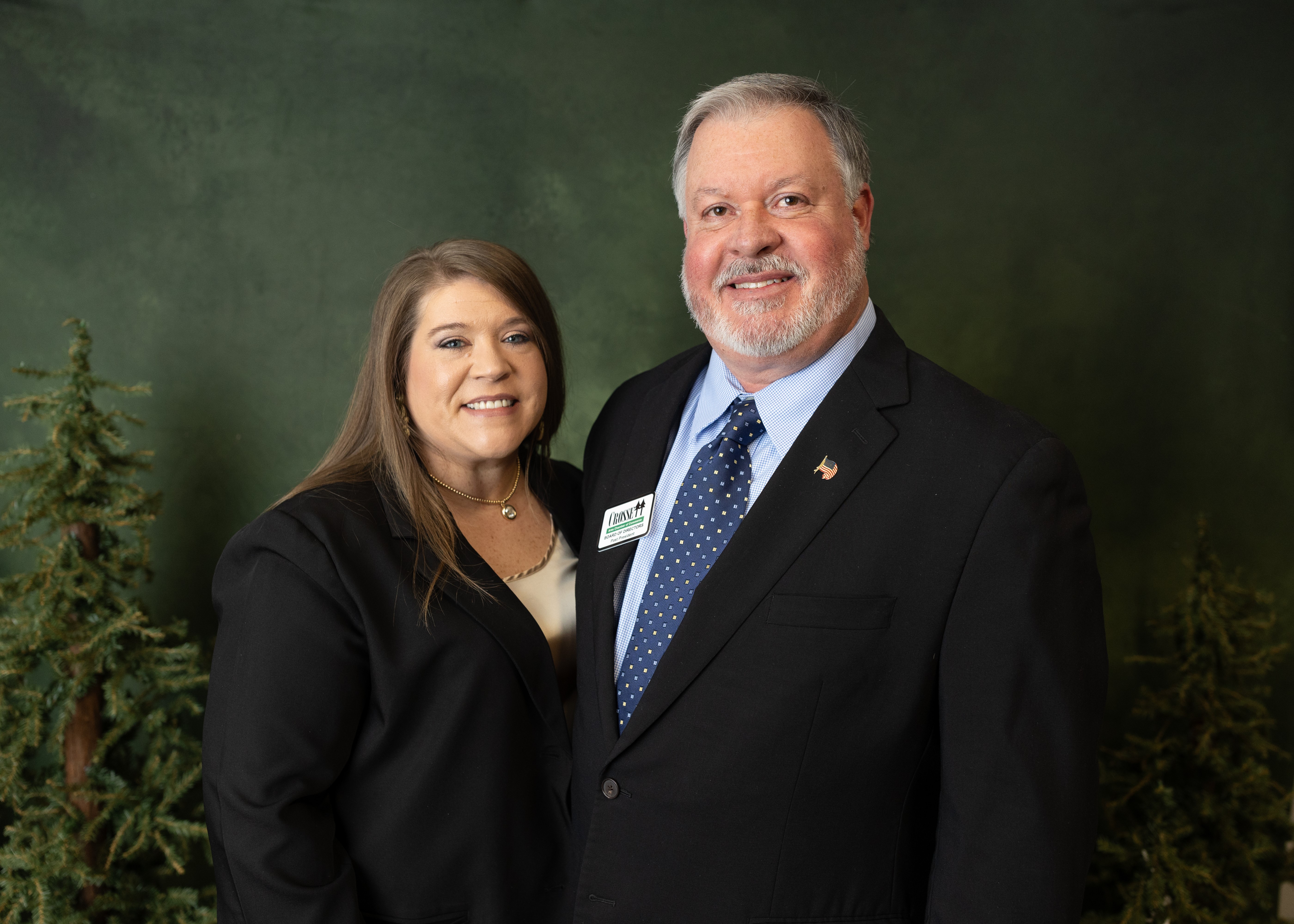 Image of Joe and his wife, Robin. Each are wearing dark suits with a background composed of trees and a dark sky.