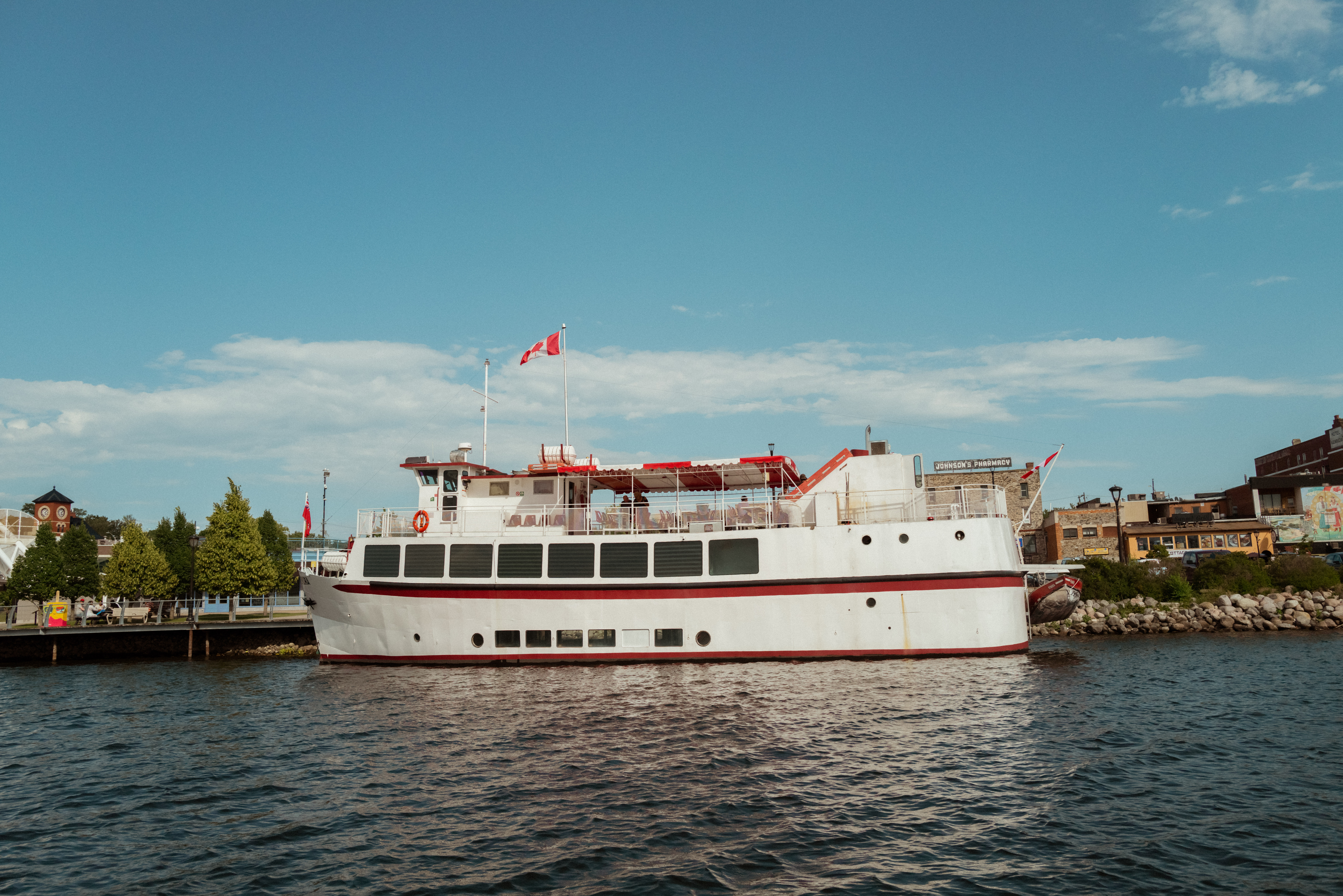 Image of a riverboat. The boat is white with red trim and has a Canadian flag flying above it.